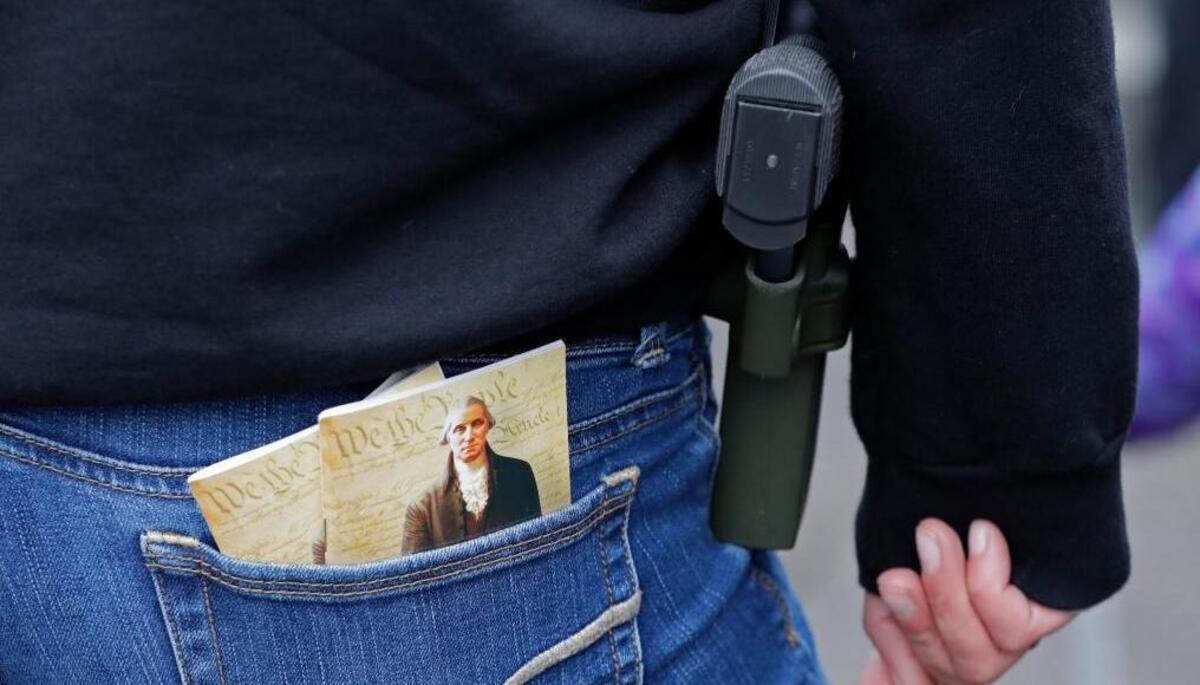 In this Jan. 12, 2018 photo, a woman wears a gun in a holster next to two copies of the U.S. Constitution during a gun rights rally at the Capitol in Olympia, Wash. A Washington state Legislature Senate committee held a public hearing Monday, Jan. 15, on several bills related to guns, including measures to prohibit high-capacity magazines and to ban so-called bump stocks, trigger modification devices designed to increase the rate of fire of a firearm.